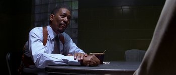 Movie still from “Kiss the Girls” (1997), directed by Gary Fleder – A man sitting at a table holding a book; Close Up shot, Low angle