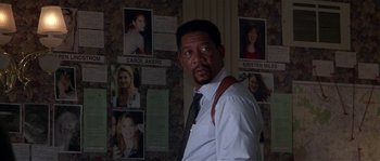 Movie still from “Kiss the Girls” (1997), directed by Gary Fleder – A man standing in front of a bunch of pictures; Close Up shot, Over the shoulder angle