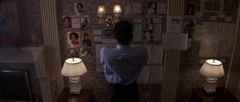 Movie still from “Kiss the Girls” (1997), directed by Gary Fleder – A man standing in front of a wall covered in pictures; Medium shot, High angle
