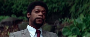 Movie still from “Klute” (1971), directed by Alan J. Pakula – A man wearing a suit and tie in front of trees; Close Up shot, Low angle