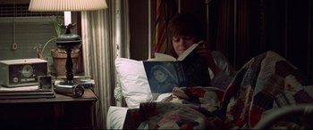 Movie still from “Klute” (1971), directed by Alan J. Pakula – A person sitting in a bed reading a book; Medium shot, High angle