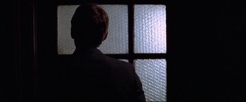 Movie still from “Klute” (1971), directed by Alan J. Pakula – A man standing in front of a window; Close Up shot, Over the shoulder angle