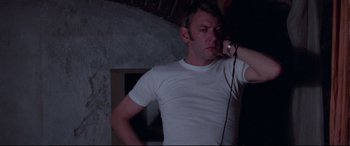 Movie still from “Klute” (1971), directed by Alan J. Pakula – A man in a white t - shirt is holding a microphone; Close Up shot, Low angle