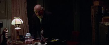 Movie still from “Klute” (1971), directed by Alan J. Pakula – An older man standing at a table with a wine glass in front of him; Medium shot, Over the shoulder angle