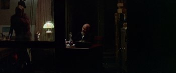 Movie still from “Klute” (1971), directed by Alan J. Pakula – A man sitting at a table in a dark room; Wide shot, Over the shoulder angle