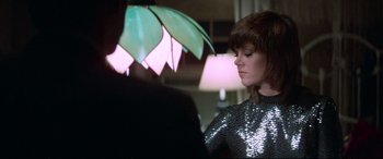 Movie still from “Klute” (1971), directed by Alan J. Pakula – A woman in a silver dress holding an open umbrella; Medium shot, Over the shoulder angle