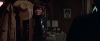 Movie still from “Klute” (1971), directed by Alan J. Pakula – A woman standing in a dark room wearing a black dress; Medium shot, Over the shoulder angle