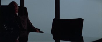 Movie still from “Klute” (1971), directed by Alan J. Pakula – A person sitting at a table in front of an open window; Medium shot, Over the shoulder angle