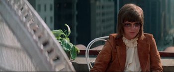 Movie still from “Klute” (1971), directed by Alan J. Pakula – A woman sitting at an outdoor table in front of a plant; Medium shot, Over the shoulder angle