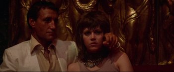 Movie still from “Klute” (1971), directed by Alan J. Pakula – A young woman wearing a necklace is sitting next to a man; Close Up shot, Low angle