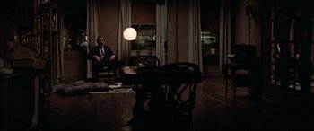 Movie still from “Klute” (1971), directed by Alan J. Pakula – A man in a suit sitting in a chair in front of a table; Wide shot, High angle