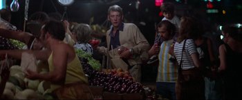 Movie still from “Klute” (1971), directed by Alan J. Pakula – A group of people standing around a table of fruit; Medium shot, Over the shoulder angle