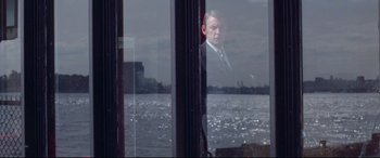 Movie still from “Klute” (1971), directed by Alan J. Pakula – A man in a suit looking out of a window; Medium shot, Over the shoulder angle