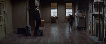Movie still from “Klute” (1971), directed by Alan J. Pakula – A man in a suit stands in an empty room with luggage; Wide shot, High angle