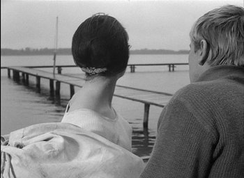 Movie still from “Knife in the Water” (1962), directed by Roman Polanski – A woman and a man sitting on a dock; Medium shot, Over the shoulder angle