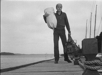 Movie still from “Knife in the Water” (1962), directed by Roman Polanski – A black and white photo of a man holding a surfboard; Wide shot, Low angle