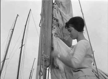 Movie still from “Knife in the Water” (1962), directed by Roman Polanski – A black - and - white photo of a woman working on a sailboat; Medium shot, Low angle