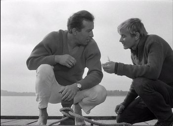 Movie still from “Knife in the Water” (1962), directed by Roman Polanski – A man and a woman sitting next to each other on a dock; Medium shot, High angle