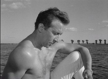 Movie still from “Knife in the Water” (1962), directed by Roman Polanski – A man sitting on top of a surfboard in the water; Close Up shot, Low angle