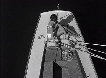 Movie still from “Knife in the Water” (1962), directed by Roman Polanski – A woman in a white bikini sitting on the side of a boat; Wide shot, Overhead angle