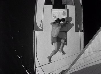 Movie still from “Knife in the Water” (1962), directed by Roman Polanski – A man laying on the deck of a sailboat; Wide shot, Overhead angle