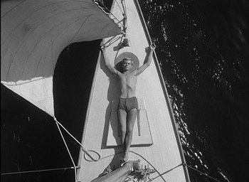 Movie still from “Knife in the Water” (1962), directed by Roman Polanski – A man laying on a sail boat in the water; Wide shot, Overhead angle
