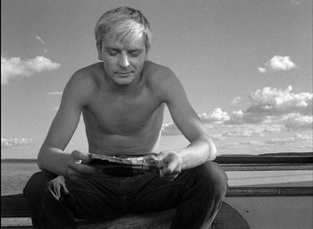 Movie still from “Knife in the Water” (1962), directed by Roman Polanski – A man sitting on the ground looking at a book; Close Up shot, Low angle
