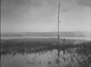 Movie still from “Knife in the Water” (1962), directed by Roman Polanski – A man standing on a dock next to a sailboat; Extreme Wide shot, Low angle
