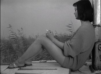 Movie still from “Knife in the Water” (1962), directed by Roman Polanski – A woman sitting on the ground holding a cigarette in her hand; Medium shot, High angle