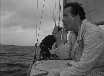 Movie still from “Knife in the Water” (1962), directed by Roman Polanski – A black and white photo of a man sitting on a sail boat; Medium shot, High angle