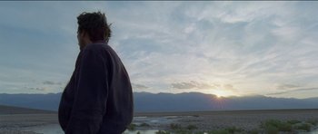 Movie still from “Knight of Cups” (2015), directed by Terrence Malick – A person looking out at the sun setting over the desert; Wide shot, Low angle