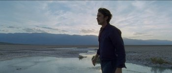 Movie still from “Knight of Cups” (2015), directed by Terrence Malick – A man standing on a beach near a body of water; Medium shot, Low angle