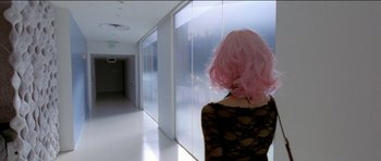 Movie still from “Knight of Cups” (2015), directed by Terrence Malick – A woman with pink hair standing in a room; Wide shot, Over the shoulder angle