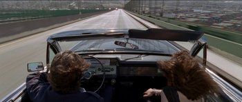 Movie still from “Knight of Cups” (2015), directed by Terrence Malick – Two people in the driver's seat of a car driving on a highway; Wide shot, High angle