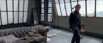 Movie still from “Knight of Cups” (2015), directed by Terrence Malick – A man standing in a living room next to a couch; Wide shot, High angle