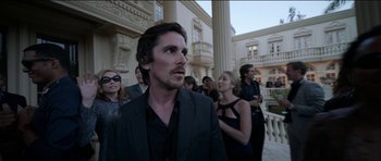 Movie still from “Knight of Cups” (2015), directed by Terrence Malick – A man in a black suit standing in front of a group of onlookers; Medium shot, Over the shoulder angle