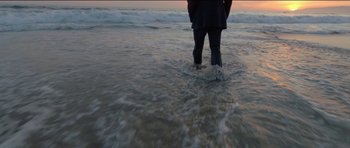 Movie still from “Knight of Cups” (2015), directed by Terrence Malick – A person standing in the water at the beach; Wide shot, High angle