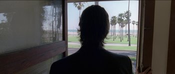 Movie still from “Knight of Cups” (2015), directed by Terrence Malick – A man looking out a window at the beach; Wide shot, Over the shoulder angle