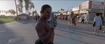 Movie still from “Knight of Cups” (2015), directed by Terrence Malick – A shirtless man holding something up to his face; Medium shot, Low angle