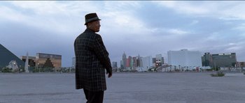 Movie still from “Knight of Cups” (2015), directed by Terrence Malick – An older man in a hat and a jacket stands in front of a city skyline; Wide shot, Low angle