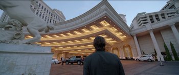 Movie still from “Knight of Cups” (2015), directed by Terrence Malick – A man standing in front of a building with cars parked in front of it; Extreme Wide shot, Low angle