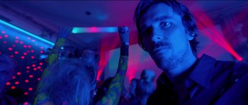 Movie still from “Knight of Cups” (2015), directed by Terrence Malick – A man in a black shirt and a crowd of people in a dark room; Close Up shot, Low angle