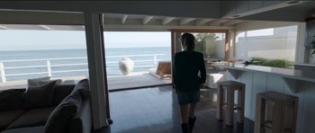 Movie still from “Knight of Cups” (2015), directed by Terrence Malick – A woman standing in front of a window looking out at the ocean; Wide shot, High angle