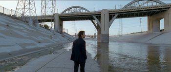 Movie still from “Knight of Cups” (2015), directed by Terrence Malick – A man standing in front of a river with a bridge in the background; Extreme Wide shot, High angle