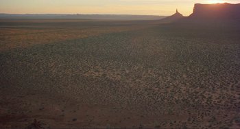 Movie still from “Koyaanisqatsi” (1982), directed by Godfrey Reggio – An aerial view of a desert landscape at sunset; Extreme Wide shot, High angle