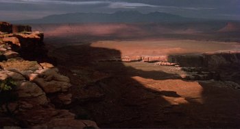 Movie still from “Koyaanisqatsi” (1982), directed by Godfrey Reggio – A view of a desert landscape with mountains in the background; Extreme Wide shot, High angle