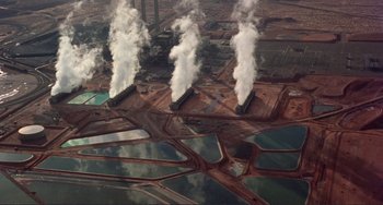 Movie still from “Koyaanisqatsi” (1982), directed by Godfrey Reggio – A group of four pipes spewing smoke into the air; Extreme Wide shot, Overhead angle
