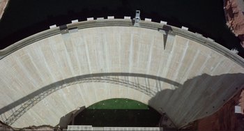 Movie still from “Koyaanisqatsi” (1982), directed by Godfrey Reggio – An aerial view of a water dam with a hole in it; Extreme Wide shot, Overhead angle