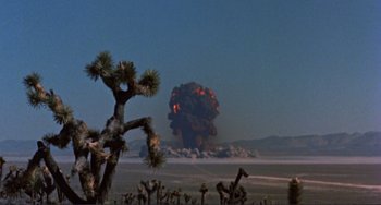 Movie still from “Koyaanisqatsi” (1982), directed by Godfrey Reggio – An explosion is seen in the background of a desert landscape; Extreme Wide shot, Low angle