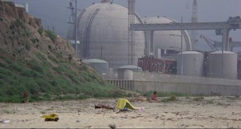 Movie still from “Koyaanisqatsi” (1982), directed by Godfrey Reggio – A tent on the beach near a cement structure; Extreme Wide shot, High angle
